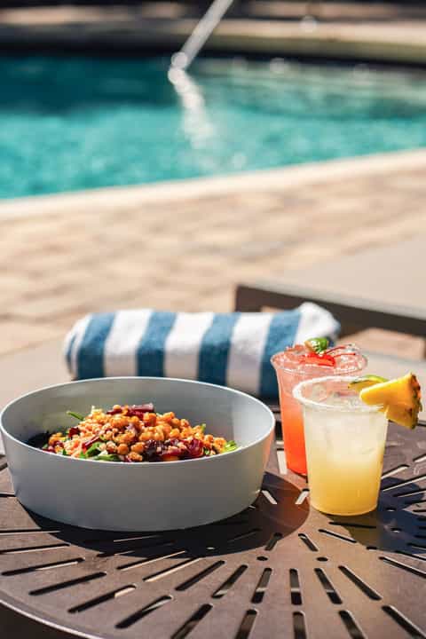 Healthy grain salad and refreshing cocktails on table overlooking resort pool