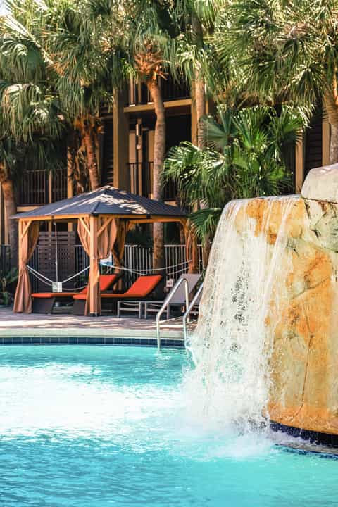 Cascading waterfall feature and wooden cabana with lounge chairs by turquoise pool