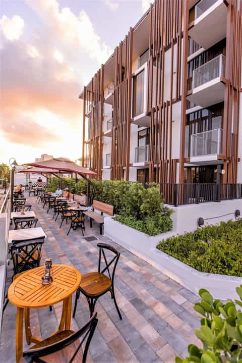Outdoor courtyard seating area at dusk with umbrellas, wooden tables, modern building facade, and landscaping