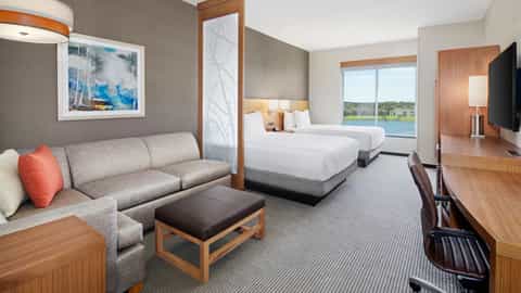 Spacious hotel suite with two queen beds, gray sofa, wood furnishings, large windows overlooking golf course