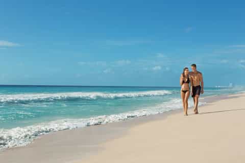 Couple walking along sandy beach with turquoise ocean waves and blue sky