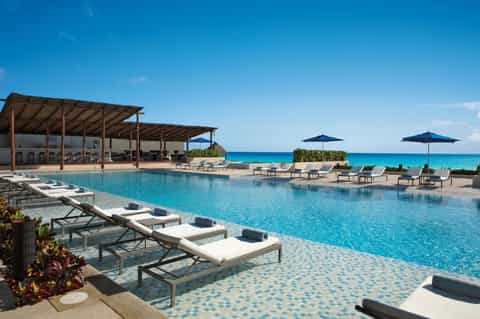 Oceanfront infinity pool with white lounge chairs, blue umbrellas, and pristine turquoise water