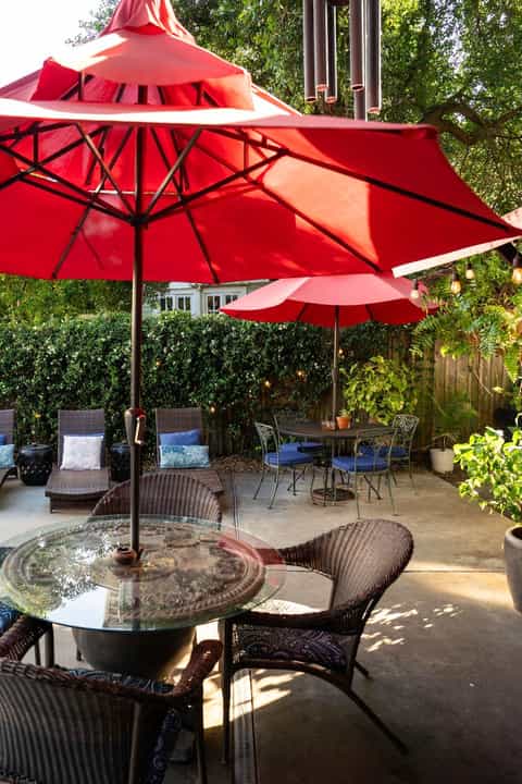 Outdoor patio with large red umbrellas, wicker chairs, and glass-top tables in a garden setting