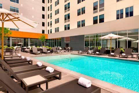 Outdoor resort pool with loungers, umbrellas, and multi-story building in bright daylight