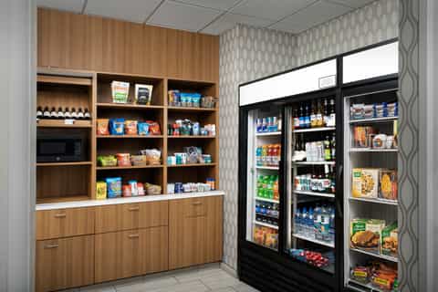 Hotel market area with wooden shelving, microwave, snacks, and refrigerated beverage coolers stocked with drinks and food.