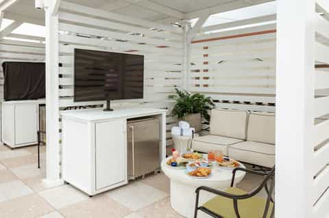 Covered outdoor lounge area with TV, mini-fridge, white furniture, and striped accent walls
