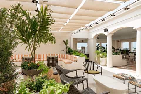 Rooftop patio with retractable shade system, striped seating, plants, and white pergola columns