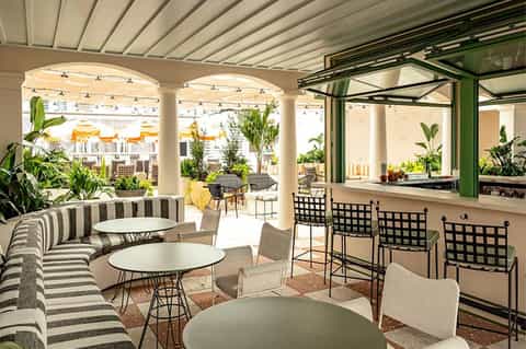 Covered outdoor bar and seating area with striped furniture, high-top chairs, and tropical plants