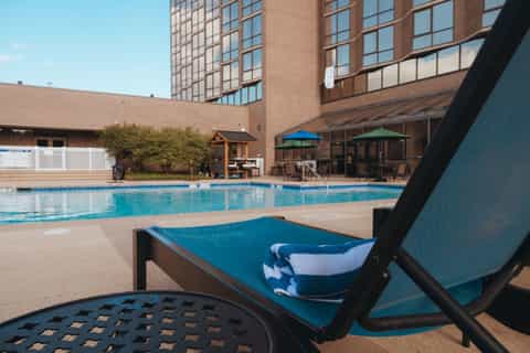 Poolside lounge chair with blue sling fabric and striped towel overlooking hotel swimming pool and brick building