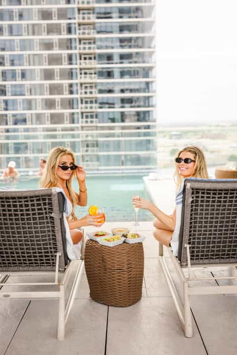 Two women relaxing on lounge chairs on rooftop terrace with city skyline view