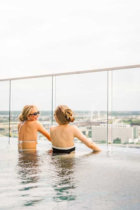 Two women in an infinity pool overlooking a cityscape from a high-rise hotel