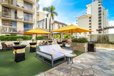 Luxury resort terrace with yellow umbrellas, lounge chairs, and apartment buildings under blue sky