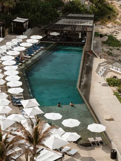Aerial view of rectangular pool with white umbrellas, blue loungers, and beachfront access
