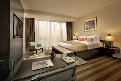 Luxury hotel bedroom with king bed, seating area, ocean view balcony, and warm lighting