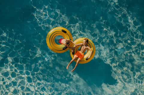 Aerial view of two children on yellow inflatable rings in crystal clear turquoise water