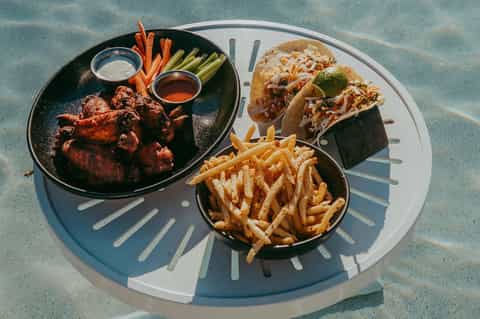 Poolside meal spread with grilled meat, tacos, fries, and fresh vegetables on concrete