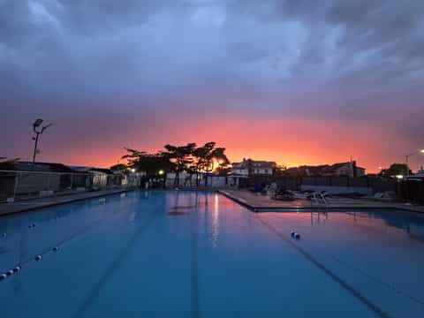 Outdoor swimming pool at sunset with colorful sky reflection and residential buildings