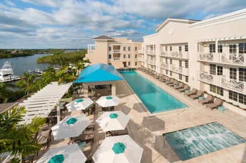 Aerial view of waterfront resort with infinity pool, lounge chairs, beach umbrellas, and river views
