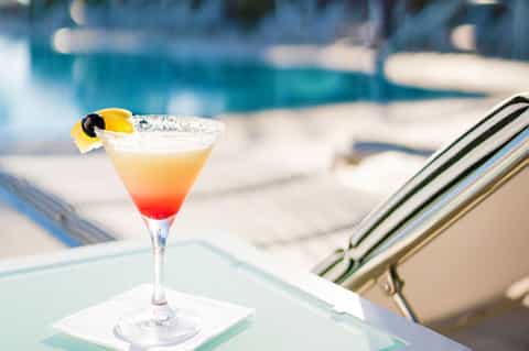 Gradient cocktail with lemon slice and black olive by pool lounge chair