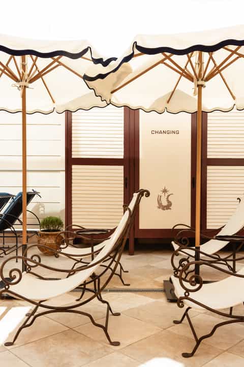 Outdoor cabana lounge area with cream umbrellas, wooden frames, and changing rooms