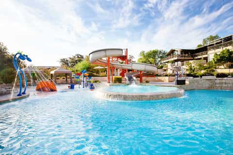 Family water park with blue slide, splash pad, and turquoise pool surrounded by resort buildings