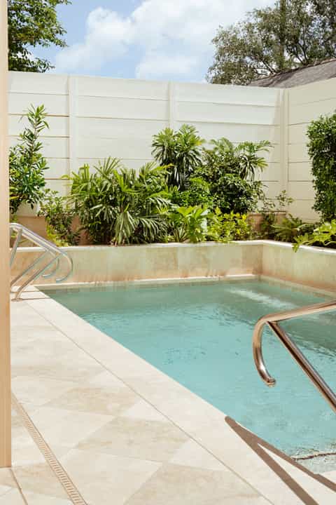 Rectangular swimming pool with turquoise water surrounded by white stone deck and tropical plants