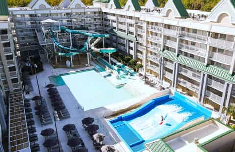 Aerial view of water park with turquoise slides, white swimming pool, black lounge chairs, and multi-story resort buildings