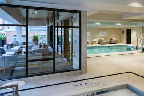 Indoor swimming pool with seating area and glass doors opening to outdoor terrace with lounge chairs