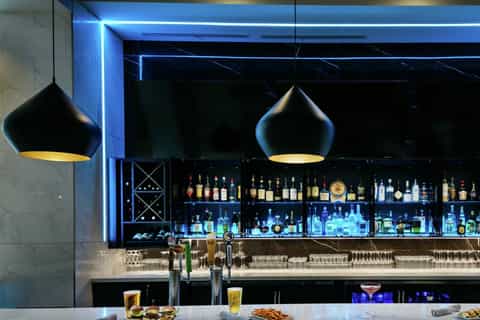 Upscale bar with blue neon lighting, pendant lamps, backlit liquor bottles, and marble countertop