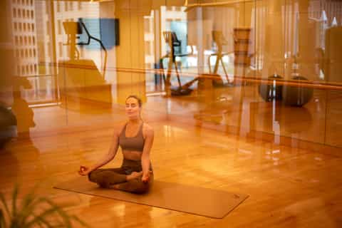 Woman practicing yoga in bright studio with mirrored walls and city views