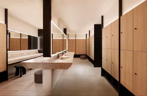 Modern spa bathroom with wooden lockers, illuminated mirrors, and stone sinks