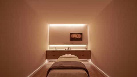 Minimalist massage room with warm lighting, wooden vanity, and comfortable massage bed