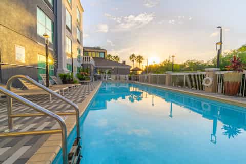 Olympic-length swimming pool with metal railings, lounge chairs, and hotel building at sunset
