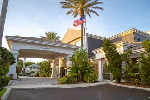 Hotel entrance with welcome canopy, American flag, palm trees, and manicured landscaping