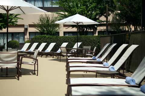 Resort pool deck with lounge chairs, umbrellas, and palm trees overlooking building facades