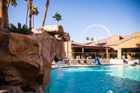 Resort pool with large Ferris wheel visible in distance, rocky landscaping and yellow buildings