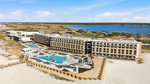 Aerial view of beachfront resort complex with pools, multi-story buildings, and coastal landscape