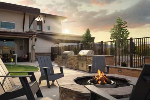 Backyard patio with fire pit, lounge chairs, stone grill counter, and modern house at golden hour