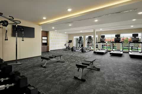 Modern fitness center with cardio equipment, strength training benches, TV screens, and large windows with views