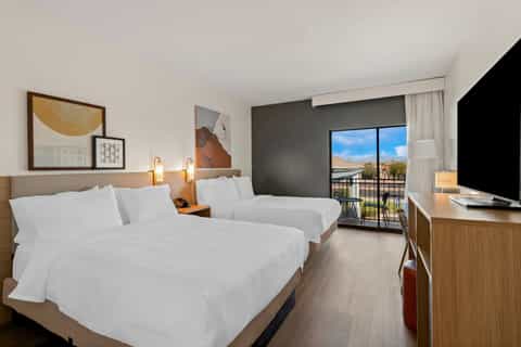 Double queen hotel room with balcony view, modern decor, and flat-screen television