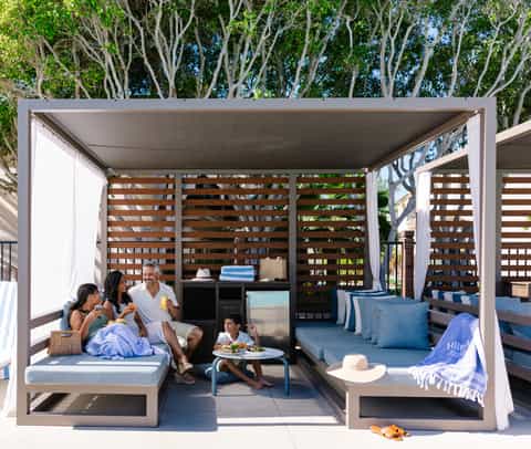 Family enjoying modern pergola cabana with blue cushioned seating and wood privacy screens
