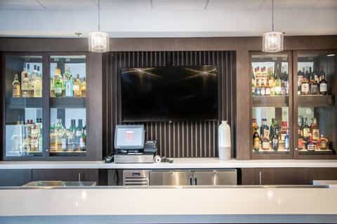 Upscale bar interior with dark wood paneling, illuminated liquor display cabinets, and flat-screen TV