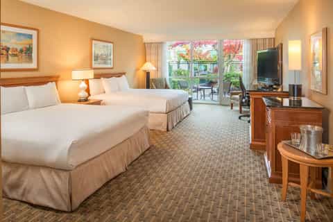 Hotel guest room with two queen beds, balcony access, flat-screen TV, and warm lighting