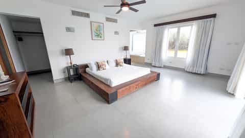 Spacious master bedroom with wooden platform bed, white tile floor, and garden views