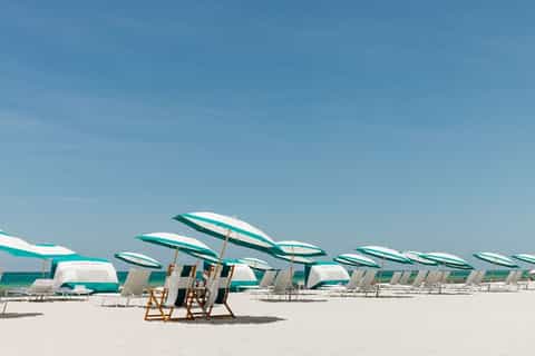 Sandy beach with rows of teal and white striped umbrellas and lounge chairs under clear sky