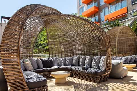 Contemporary woven pod lounge seating with curved design, cushions, and yellow side table on terrace