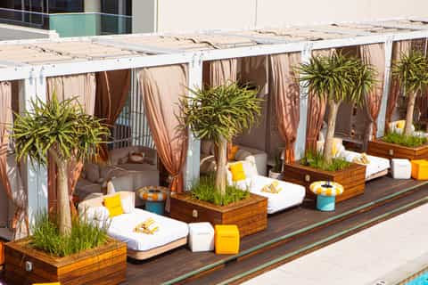 Luxury poolside cabanas with white daybeds, striped curtains, and potted plants along deck