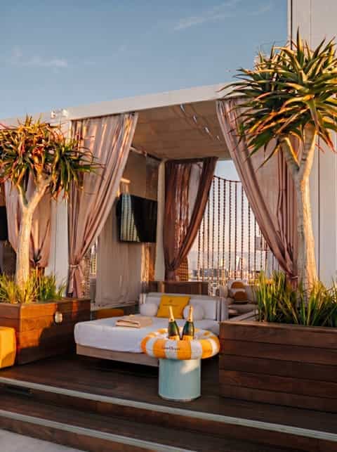 Upscale resort cabana with white daybed, sheer curtains, potted plants, and branded ice bucket