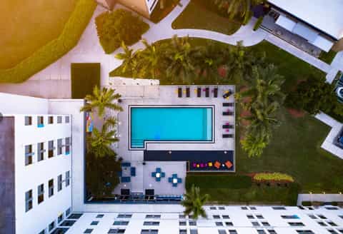 Aerial view of resort pool surrounded by landscaping, seating areas, and modern white buildings