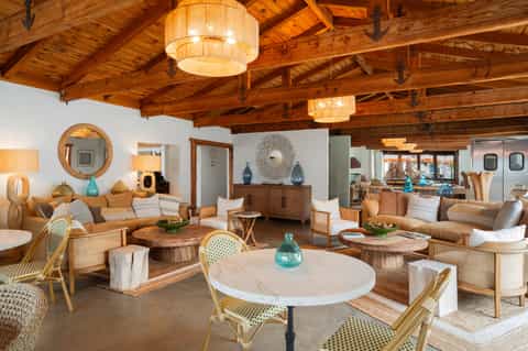Spacious mid-century modern living room with exposed wooden beams, marble tables, rattan chairs, and turquoise accents